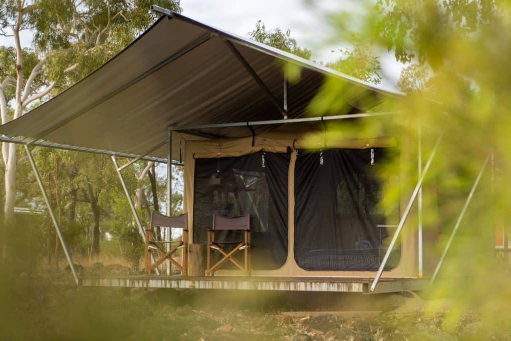 Eco-style canvas safari tent with a tin roof, set in the Australian bush, featuring canvas chairs on a raised timber deck.